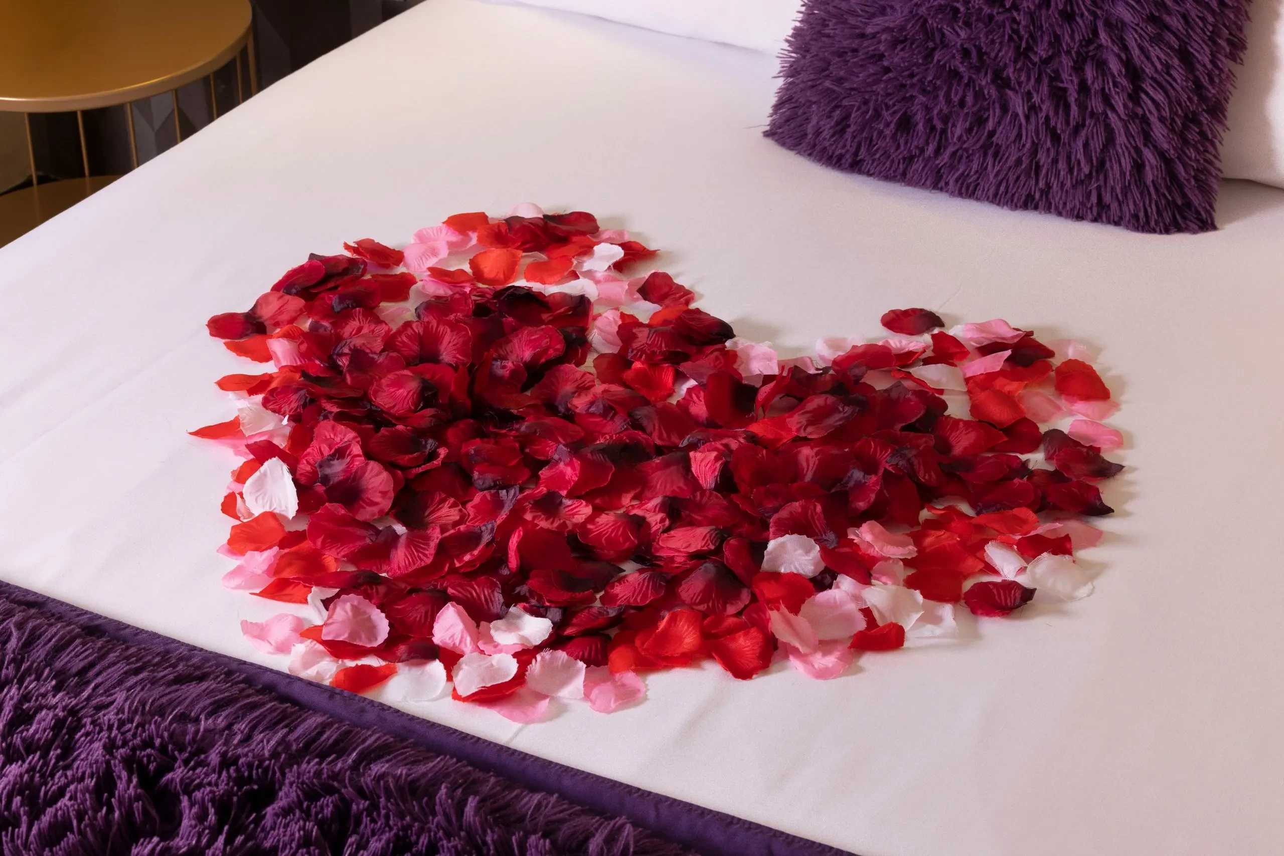 Pétales de rose rouges en cœur sur le lit.
